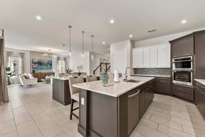 A modern kitchen with dark cabinetry, a central island, and built-in appliances. - Sanctuary at Bears Den, Near Disney, Private Pool, Luxury Golf (Kissimmee)