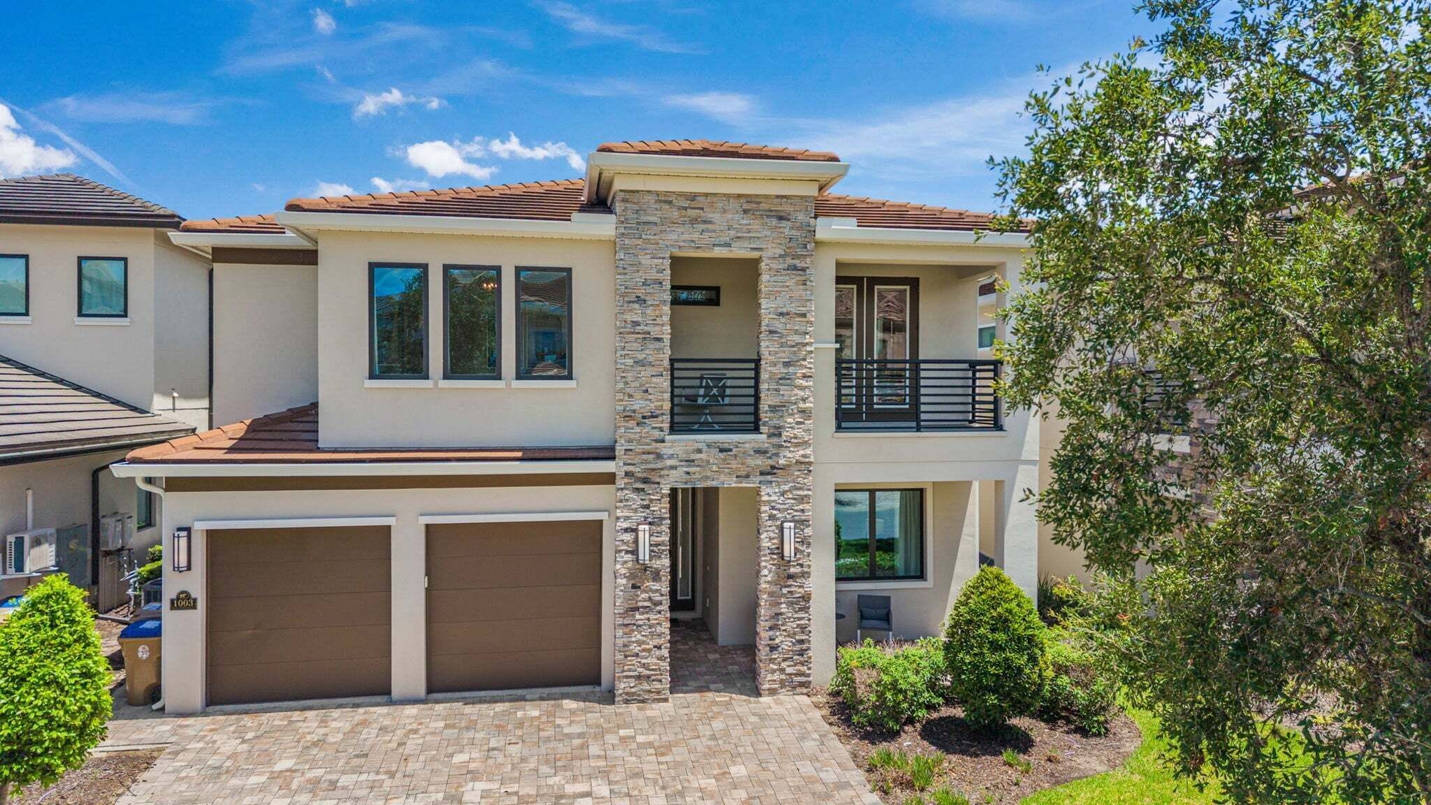 Ein zweigeschossiges Haus mit einer Steinfassade, einer Garage und einem Balkon.