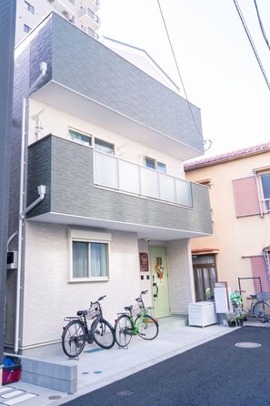 A two-story residential building with a balcony on the upper floor, a green door, and bicycles parked outside. - SunShine Terrace 晴空台 · Full Apartment · Free parking (Toshima City)