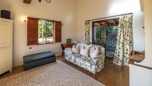 Ein gemütliches Wohnzimmer mit einer Couch, einer Bank, einer Chandelier und Blick auf Grün hinter den Fenstern.