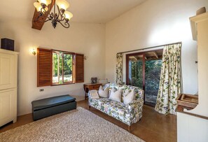 Ein gemütliches Wohnzimmer mit einer Couch, einer Bank, einer Chandelier und Blick auf Grün hinter den Fenstern.