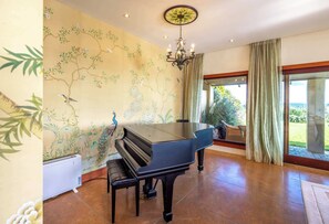 Une pièce avec un grand piano, un lustre et une grande fenêtre avec des rideaux.