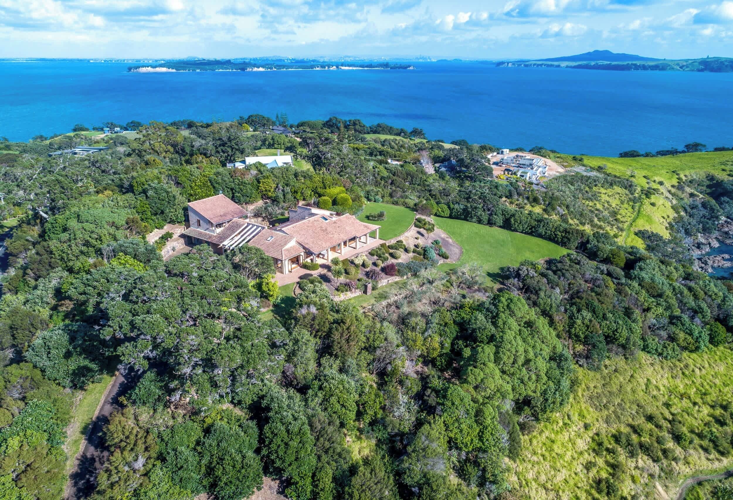 A large estate with multiple buildings, surrounded by dense greenery and a view of the sea.
