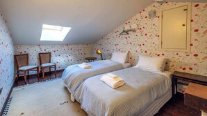 Ein Schlafzimmer mit zwei Betten, einem Oberlicht, einem Sessel, einem kleinen Tisch und floralem Wandpapier.