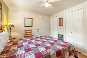 A bedroom with a bed, a chair, a ceiling fan, and two doors.