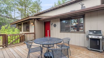 A deck with a round table and chairs, a red door, and a Weber Spirit grill.