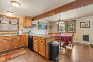 Une cuisine avec des meubles en bois, un lave-vaisselle, une fenêtre avec des rideaux, un coin repas avec une table et des chaises, et un ventilateur de plafond.