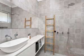 Un baño con un lavamanos grande y blanco, un espejo, una ducha y una escalera de madera.