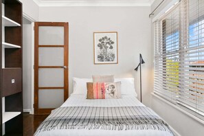 A bedroom with a bed, a framed picture on the wall, a window with blinds, and a door with a frosted glass panel. - WAV64 - Charming Waverton Escape | Top-Floor 2-Bed With City & Harbour Views (Waverton)