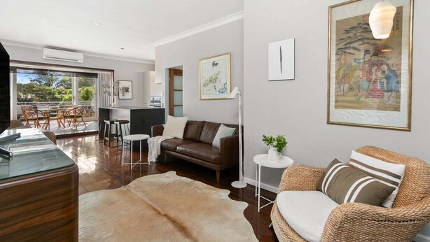 A modern living room with a leather sofa, a glass coffee table, and a woven armchair. There is a dining area with a table and chairs, and a large window providing a view of the outdoors. - WAV64 - Charming Waverton Escape | Top-Floor 2-Bed With City & Harbour Views (Waverton)