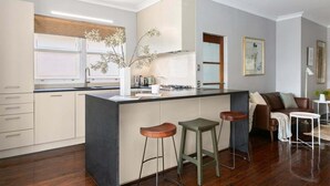 A modern kitchen with a central island, bar stools, and a seating area with a sofa and coffee table. - WAV64 - Charming Waverton Escape | Top-Floor 2-Bed With City & Harbour Views (Waverton)