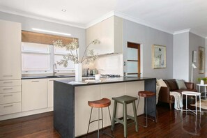 A modern kitchen with a central island, bar stools, and a seating area with a sofa and coffee table. - WAV64 - Charming Waverton Escape | Top-Floor 2-Bed With City & Harbour Views (Waverton)