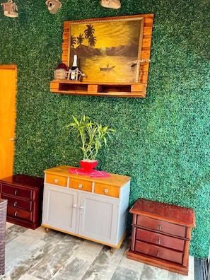 Quarto com parede verde, um armário de madeira, uma mesinha com uma planta e um quadro sobre o armário.