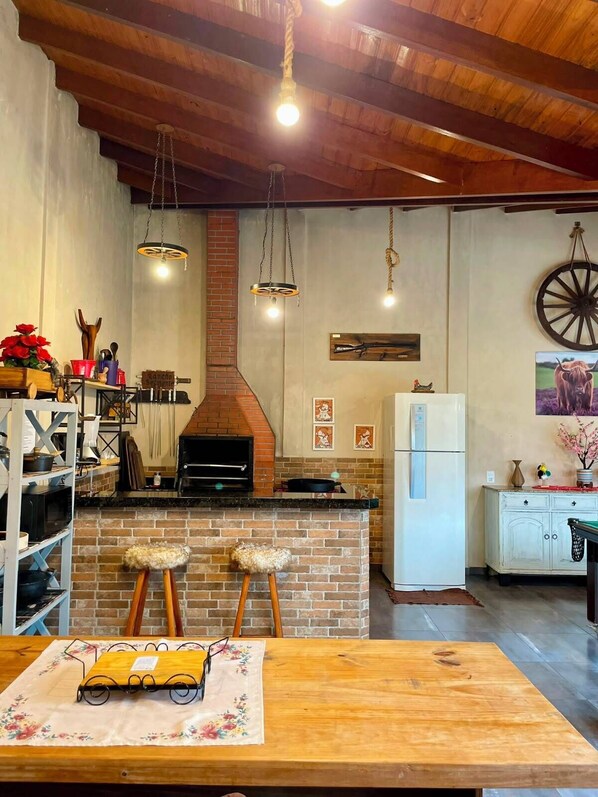 A kitchen with a brick fireplace, hanging lights, and a rustic wooden ceiling.