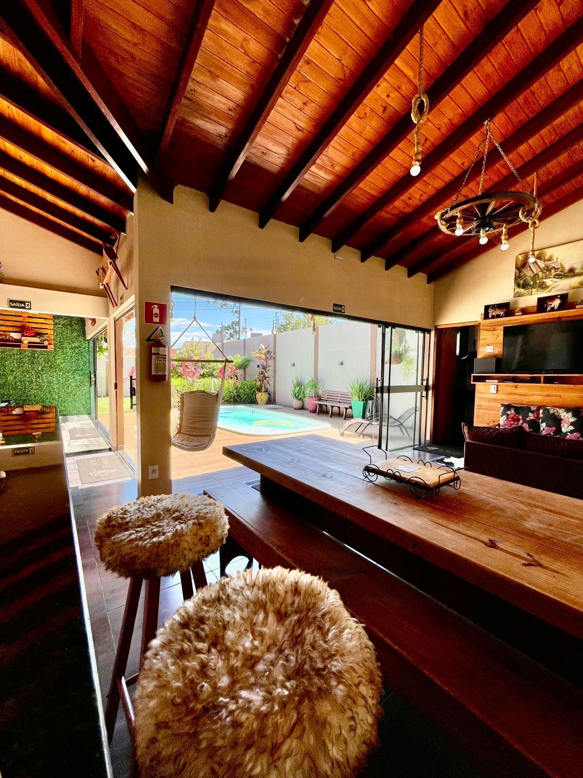 A modern interior with a wooden ceiling, a pool visible through the glass door, and a bar area with stools.