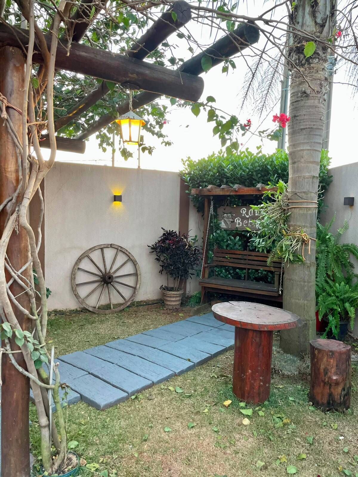 A garden with a wooden bench, a wooden table, a wheelbarrow, and a planter with plants.