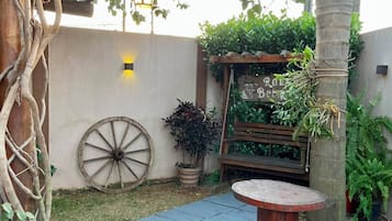 A garden with a wooden bench, a wooden table, a wheelbarrow, and a planter with plants.
