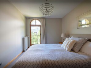 Une chambre à coucher avec un grand lit, un lustre, une fenêtre avec des rideaux et un tableau au mur.
