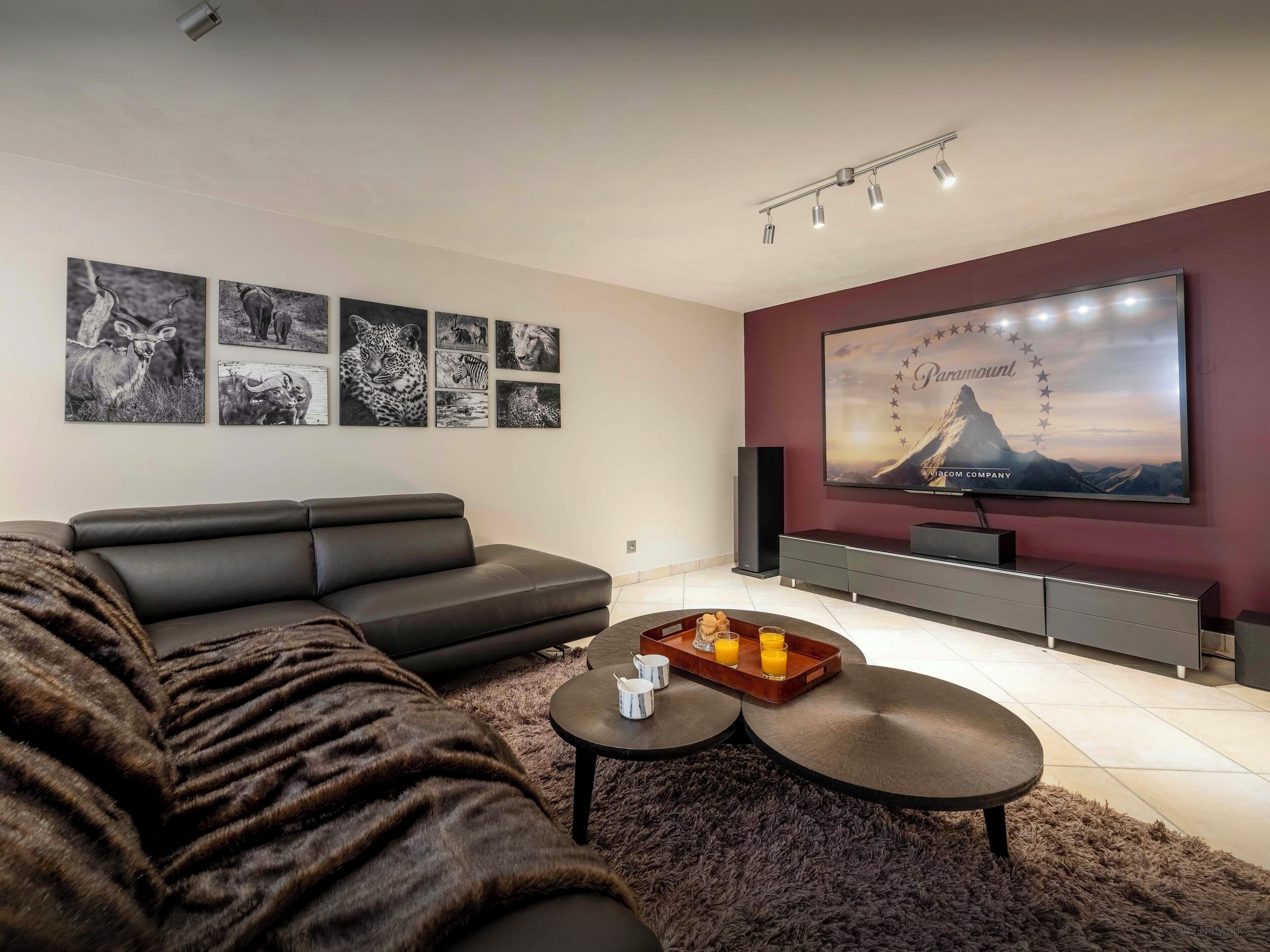 Una sala de estar moderna con un sofá seccional, un televisor de pantalla plana montado en la pared y una mesa de centro con una bandeja de jugo de naranja.