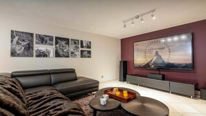 A modern living room with a sectional sofa, a flat-screen TV mounted on the wall, and a coffee table with a tray of orange juice.
