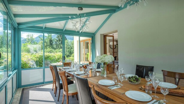 A dining area with a table set for four, large windows, and a view of greenery.