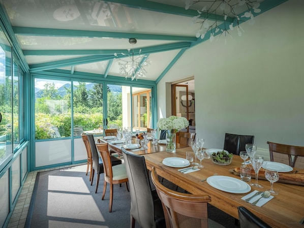 A dining area with a table set for four, large windows, and a view of greenery.