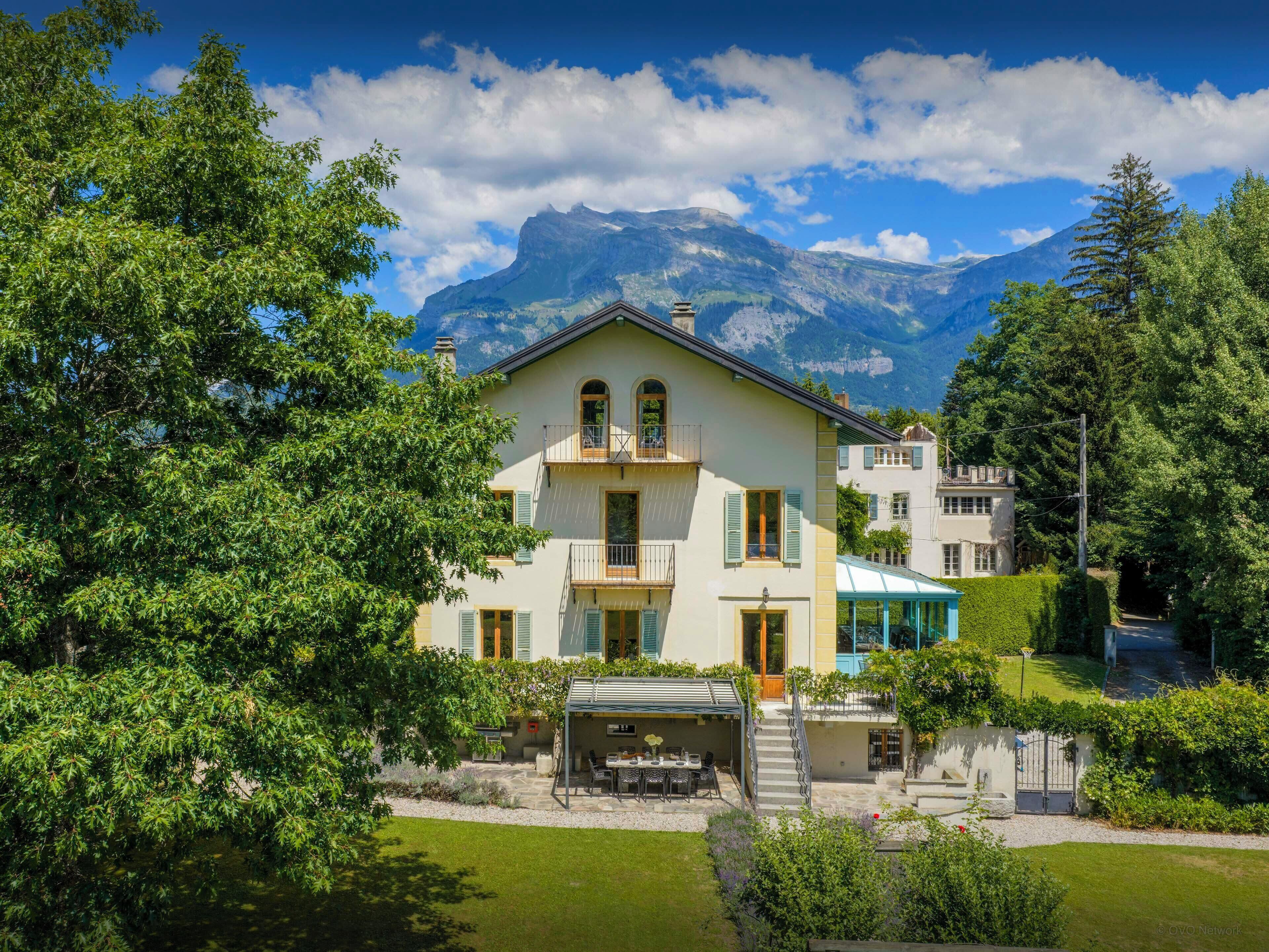 Ein zweistöckiges Haus mit Balkon, überdachter Terrasse und Blick auf die Berge.