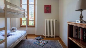 A room with a bunk bed, a radiator, a bookshelf, and a window with a view of greenery.