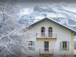 A two-story building with a balcony, a mountain backdrop, and snow-covered trees.