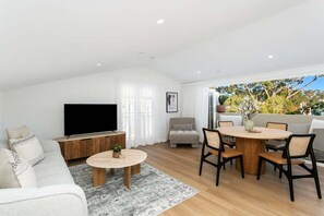 A modern living room with a flat-screen TV, a sofa, a coffee table, and a dining area with chairs. - FITZ2 - Kirribilli Comfort | 2-Bed Apartment With Harbour Views (Kirribilli)