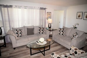 A living room with two sofas, a glass coffee table, and a lamp. - St. Pete Getaway - Spacious 4-bedroom house (St. Petersburg)