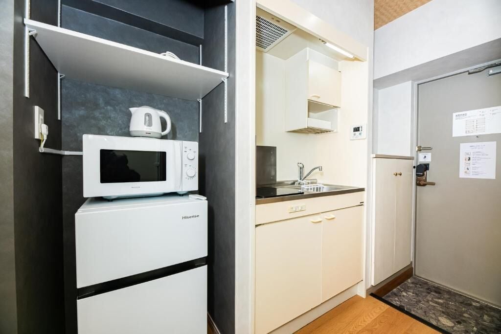 Una kitchenette compacta equipada con microondas, un refrigerador pequeño y un lavamanos.