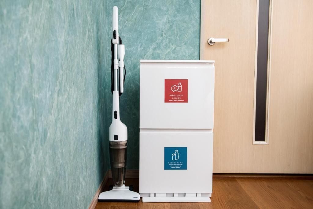 Un aspirador junto a un armario blanco con etiquetas de reciclaje y conservación del agua.