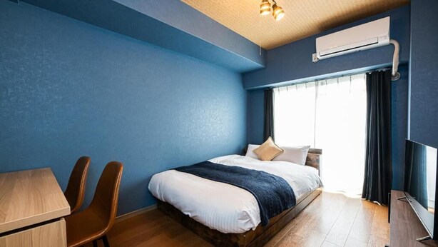 Quarto com cama, escrivaninha, cadeiras, televisão e ar condicionado.