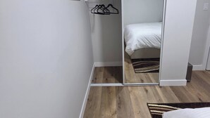 Ett sovrum med en säng, ett trägolv, en garderob med en spegel och en klädstång.