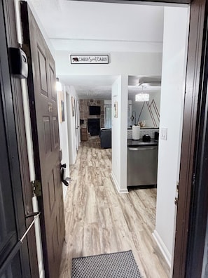 A hallway leading to a cabin labeled 'CABIN Sweet Cabin' with a stone wall, wooden flooring, and a kitchen area visible in the distance. - 2bd/2bth/3Pools/BearSightings (Gatlinburg)