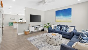 A modern living room with a flat-screen TV, a blue sofa, a patterned ottoman, and a large painting on the wall. - Isla Ohana: Key Largo, Jacuzzi, Private Yard, Playset, BBQ (Key Largo)