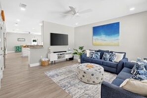 Uma sala de estar moderna com televisão de tela plana, um sofá azul, um banquinho estampado e um quadro grande na parede.