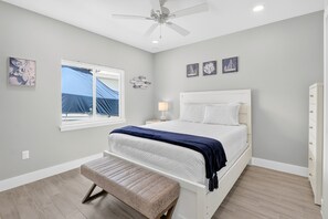 Quarto com cama, um banquinho, ventoinha no teto, janela e decorações nas paredes.