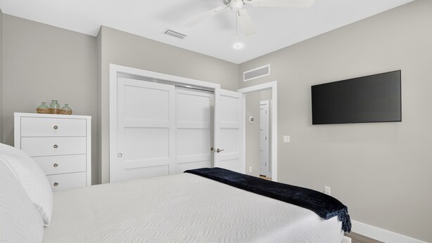 A bedroom with a bed, dresser, wardrobe, ceiling fan, and a TV mounted on the wall. - Isla Ohana: Key Largo, Jacuzzi, Private Yard, Playset, BBQ (Key Largo)