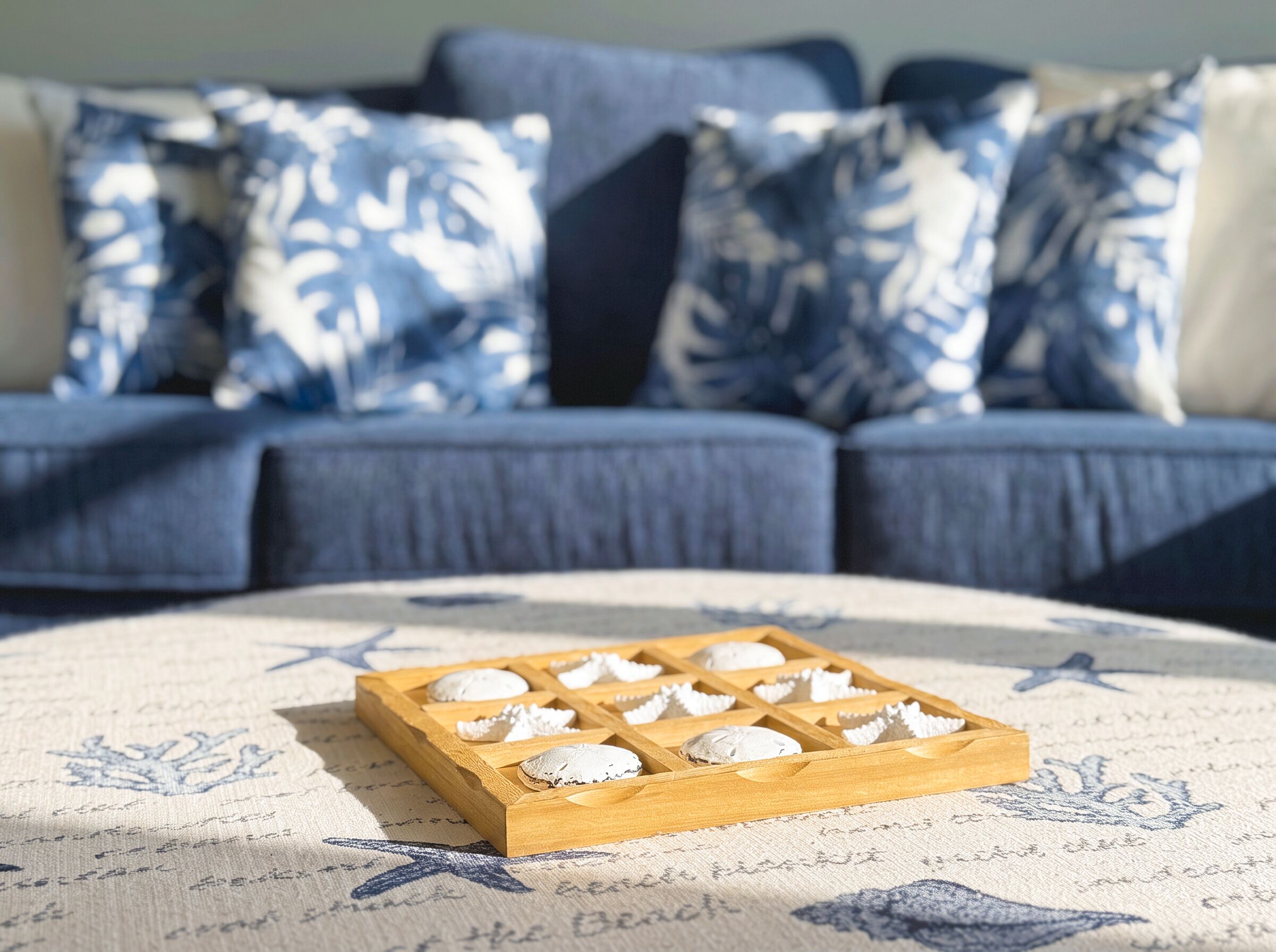 A wooden tray with cookies on a patterned rug, in front of a sofa with blue and white pillows.