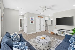 Una sala de estar moderna con un sofá gris, una mesa de centro, un televisor de pantalla plana y un ventilador de techo.