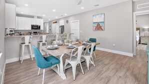 A modern kitchen with white cabinets, a microwave, and a dining area with a wooden table set for four. - Isla Ohana: Key Largo, Jacuzzi, Private Yard, Playset, BBQ (Key Largo)