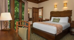 Habitación de hotel con una cama de madera, un escritorio con lámpara y vistas al exterior con vegetación.