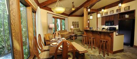 A spacious dining area with a high ceiling and wooden beams, a cozy living room with a fireplace, and a kitchen with a stone backsplash.
