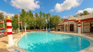 En swimmingpool med et forbudsskilte mod dykning, omgivet af liggestole og en bygning med en rød og hvid facade.
