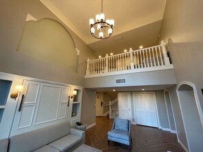 A spacious living area with a high ceiling, a chandelier, a staircase with a railing, and a view to a second floor. - Orlando | Large Family Retreat | Pool + Spa | 3BR Sleeps 12 (Lake Buena Vista)