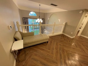 A room with a wooden floor, a sofa, a white railing, and a view of the outdoors. - Orlando | Large Family Retreat | Pool + Spa | 3BR Sleeps 12 (Lake Buena Vista)