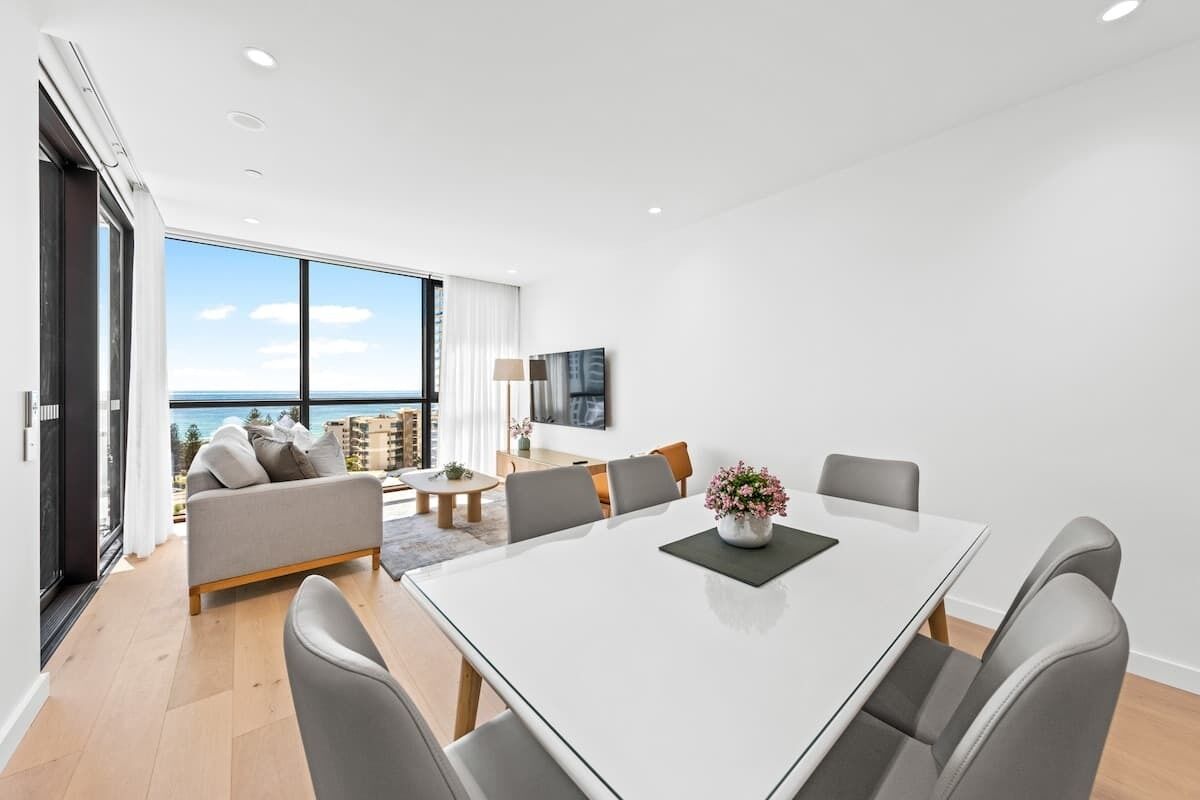 A modern hotel room with a large balcony, a dining area with a white table, and a sofa.
