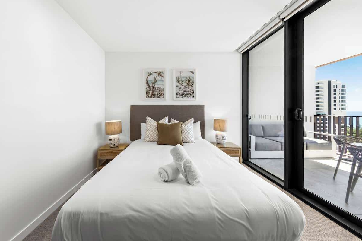 A hotel room with a large bed, two bedside tables with lamps, a balcony with a chair, and artwork on the wall.
